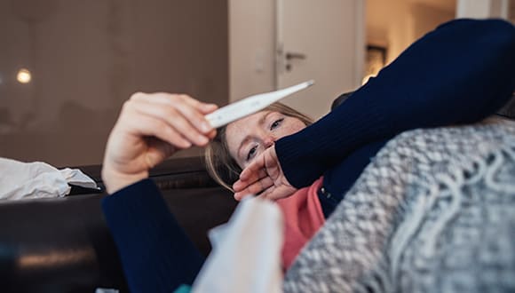 A person taking their temperature with a digital thermometer