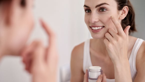 A woman applying skin care product to his face