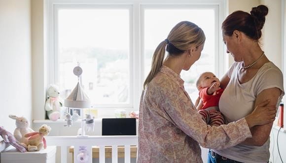 Mother with signs of postnatal depression standing with friend and looking at newborn baby