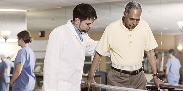 Male doctor aiding a middle aged man walk between two beams